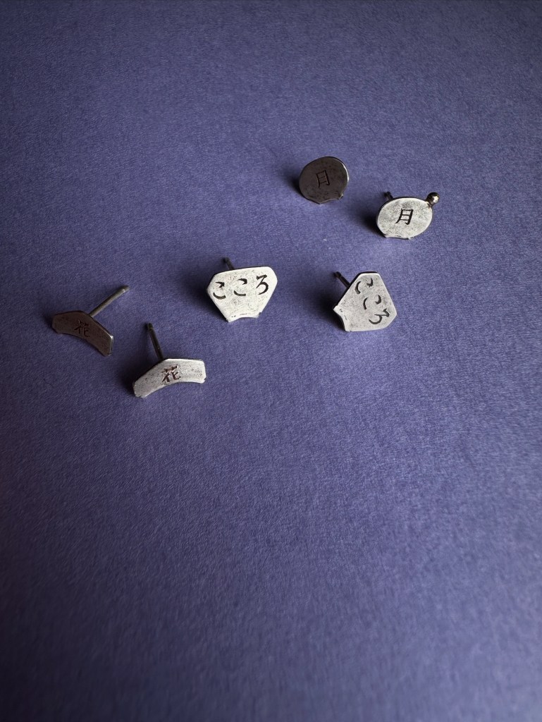 Bijoux en argent avec des inscriptions japonaises, disposés sur un fond violet.