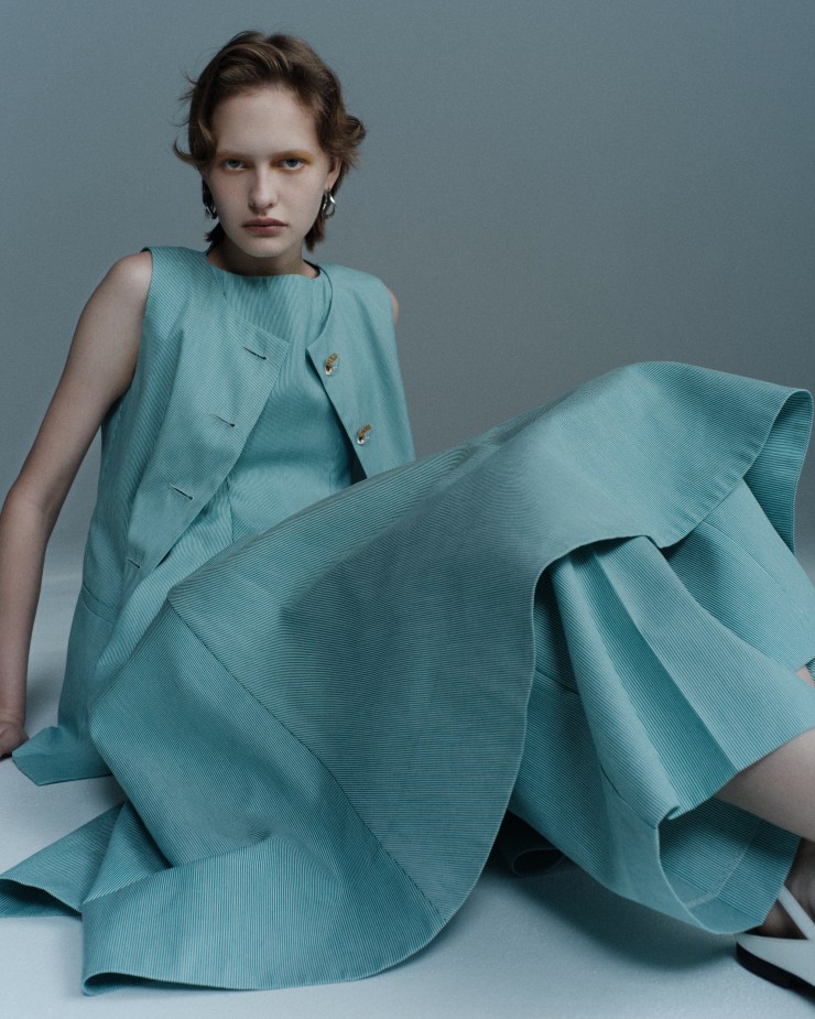 Modèle portant une robe et un gilet bleu clair sur fond neutre, affichant une expression confiante.