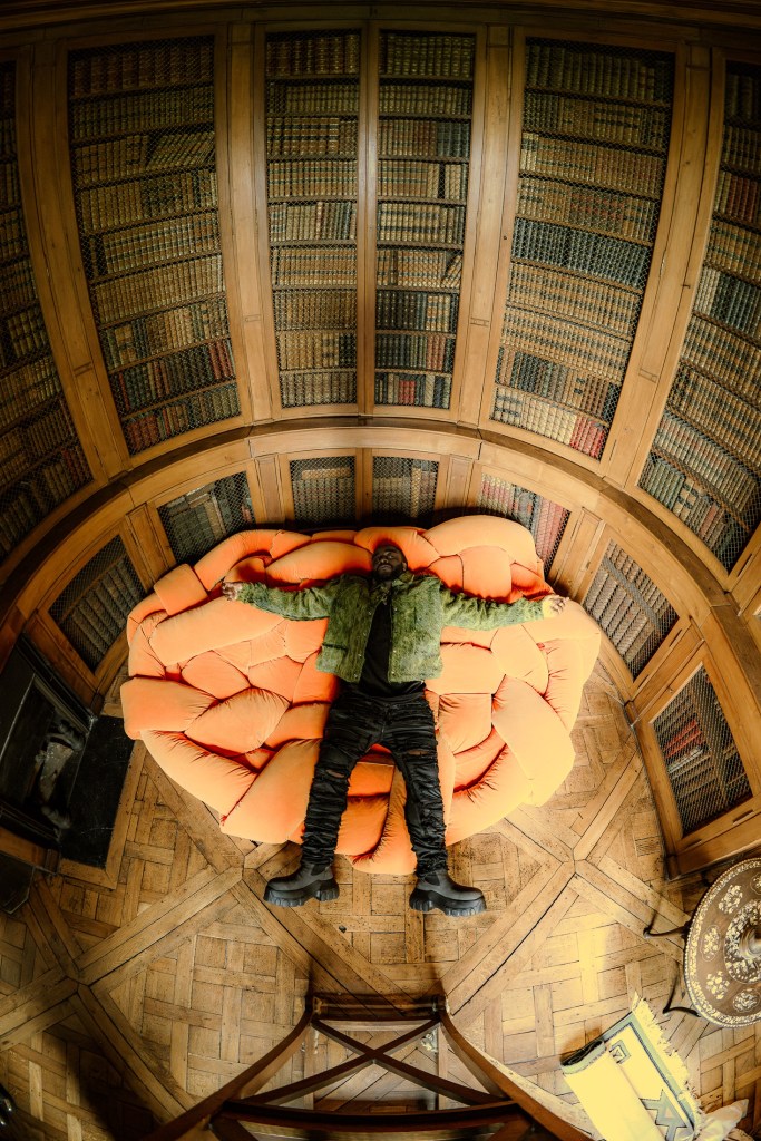 Un homme allongé sur un canapé orange dans une pièce avec des étagères de livres en bois, vue d'en haut.