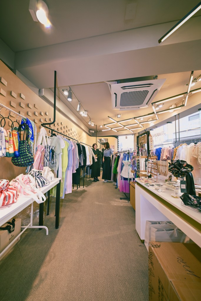 Intérieur de la boutique SHOP JINJJA à Séoul, montrant des vêtements colorés accrochés sur des portants et des accessoires exposés sur des tables.