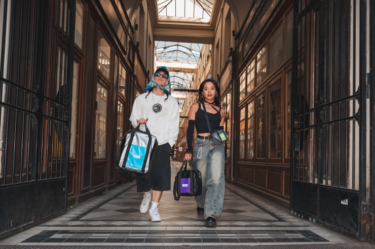 Deux modèles marchent dans un passage parisien, portant des sacs de la marque Way Back Home, entourés d'architecture élégante.