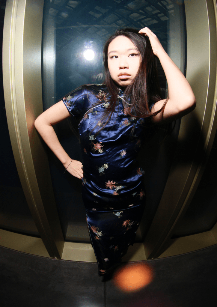A young woman poses confidently in a blue satin dress with floral patterns.