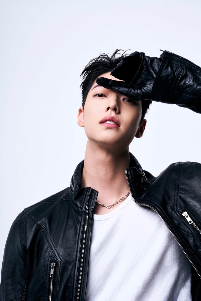 A young man wearing a black leather jacket and a white shirt, striking a stylish pose while partially covering his face with a black leather glove.