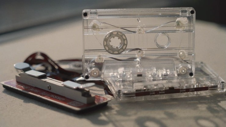 A transparent audio cassette with a partially unwound tape and a cassette shell lying on a surface, accompanied by a cassette player.
