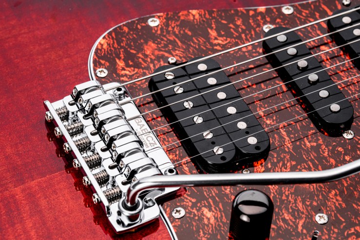 Close-up of an electric guitar bridge and pickups featuring a red and black tortoiseshell pickguard.