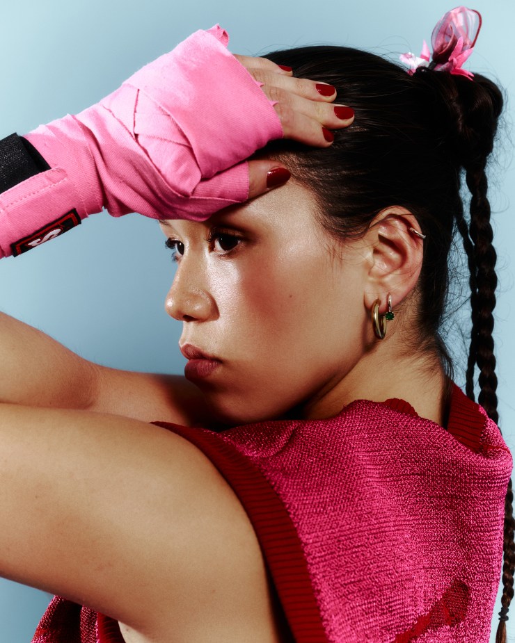 Profile of an athlete with pink hand wraps, wearing a red sleeveless top, looking intently to the side with a focused expression.