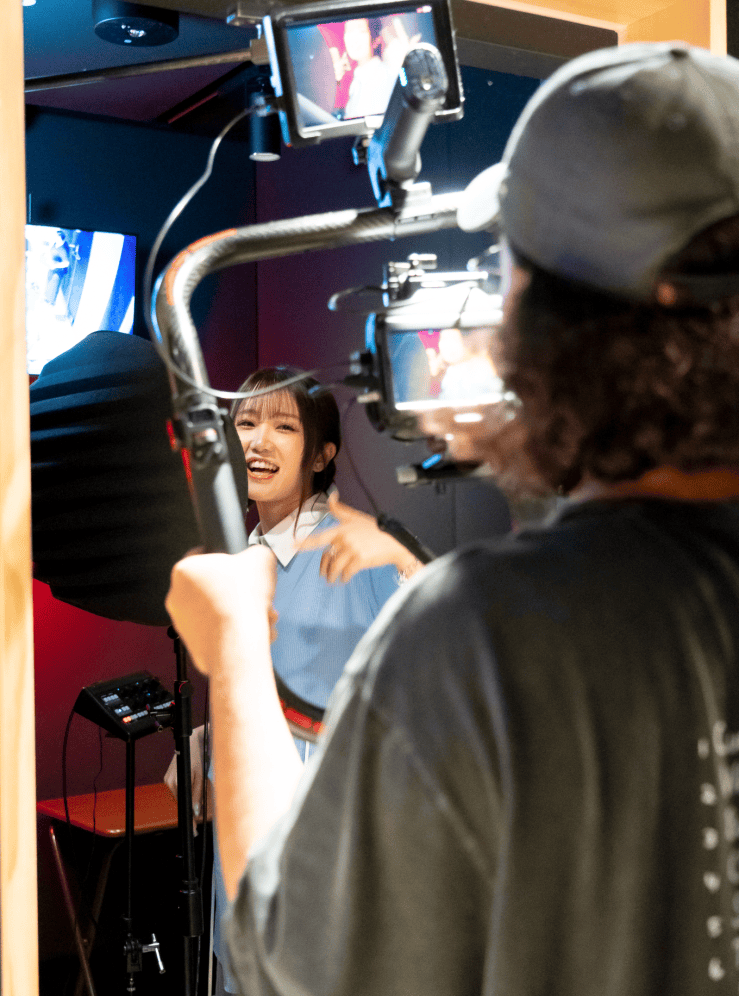 A young woman smiling and gesturing in a recording studio while being filmed by a person holding a camera rig.